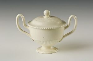  A carefully crafted off-white porcelain sugar bowl with a lid, featuring embossed dotted details and gracefully curved handles, set against a plain background to highlight its elegant design. Artist name and title are unknown.