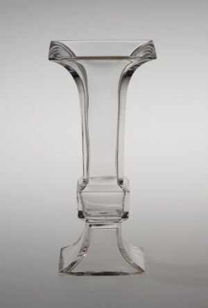  A symmetrical clear glass vase or stand with a fluted top, narrowing neck, widened midsection, and flared base, set against a gradient grey background.