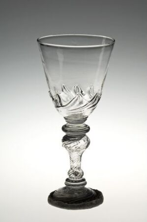  A clear glass goblet with intricate floral patterns etched into the bowl, a decorative sphere in the middle of the stem, and a solid disc-shaped base, displayed against a gradient white-to-light gray background.