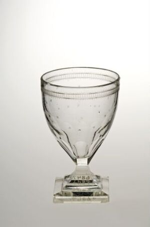  A clear hand-blown glass goblet with a wide bowl and square base, featuring tiny air bubbles throughout, set against a soft white-to-gray gradient background.