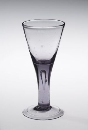  A tall, clear crystal glass with a slight purple tint, featuring a tapered design and a round base, set against a light gray background. The glass is empty and captures light, emphasizing its transparent and reflective quality. Artist and title are unknown.