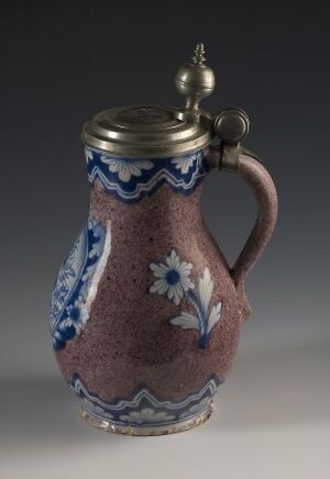  A brownish-pink ceramic pitcher with blue and white floral patterns and a metal lid positioned against a dark gray to black gradient background.