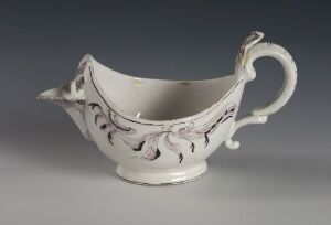  A white-glazed faience sauce boat with hand-painted manganese red decor, crafted by Herrebøe Fajansefabrikk, placed against a smooth grey background.