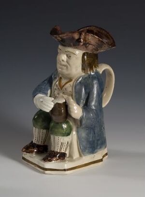  A novelty ceramic mug designed in the shape of a cheerful, seated man wearing a brown hat and blue coat, holding green and brown bottles, with a detailed handle at his back.