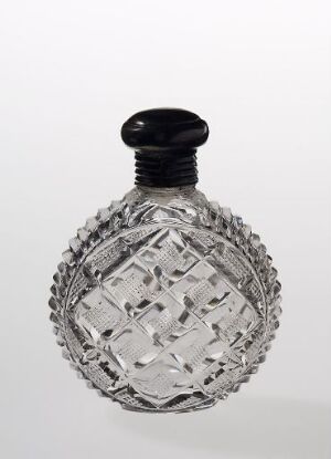  A transparent, intricately cut glass perfume bottle with a rounded black stopper against a light grey background.