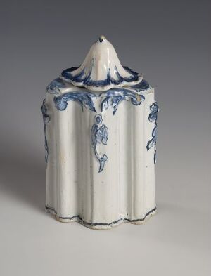  A glazed faience item titled "Thee-Daase" by an unknown artist, featuring a white, vertically fluted body with a matching conical lid, both adorned with hand-painted cobalt blue decorative elements.