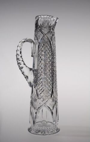  Tall and elegant slipt krystall pitcher by Hadeland Glassverk with intricate diamond-shaped patterns and a twisted handle, set against a graduated grey background.