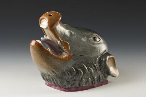  A whimsical gray ceramic hippopotamus figurine with detailed eyes and textured skin, its open mouth containing a glossy orange-brown bird, all set against a simple background, resting on a narrow purple base.