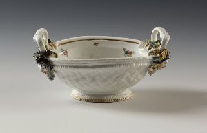  An elegant neoclassical porcelain bowl from the Sulkowsky service set, featuring a textured exterior resembling basketweave, a gold-rimmed top, and two decorative masks adorned with gilded leaves serving as handles, set against a light grey background.