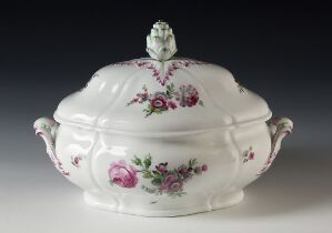  A white porcelain tureen with a lid, decorated with hand-painted pink, purple, and green floral designs and a vegetal finial on the lid. The tureen features elegant curves and raised sections, with sculpted comfortable handles on each side.