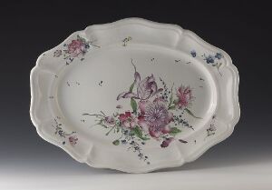  An oval ceramic platter with scalloped edges, featuring hand-painted floral designs in shades of pink, purple, and blue with green foliage on a creamy white background, against a neutral gray backdrop.