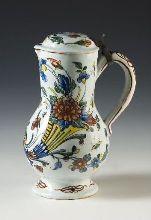  An ornately decorated ceramic pitcher with a white base and vibrant floral pattern in blue, yellow, green, and brown hues against a neutral gray background. Artist name and title are unknown.