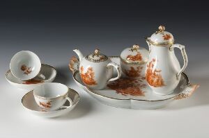  A porcelain tea set with rust-colored floral patterns and gold accents, including a teapot, sugar bowl, creamer, two cups with saucers, and a serving tray, displayed on a light background. Artistname and title are unknown.