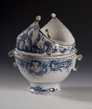  A white-glazed faience serving bowl with hand-painted cobalt blue designs and worn gold detailing. The bowl has a dome-shaped lid with a finial and scroll-shaped side handles. The intricate blue patterns are botanical and possibly heraldic in nature, and the bowl stands out sharply against a dark, neutral background. Artist Name: Ukjent (Unknown). Title: Unknown.