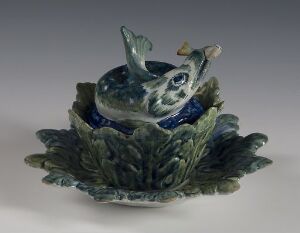  A ceramic sculpture of a whimsical blue squirrel nestled in a green leafy base, with expressive eyes and textured fur, against a neutral background. Artist and title unknown.