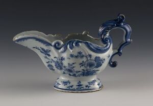  An elegant porcelain sauce boat with a high-arcing, scroll-shaped handle and intricate blue floral patterns on a white background. Artist name and title are unknown.