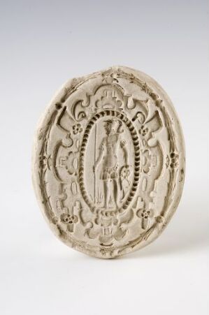  An oval-shaped, embossed plaque with a classical figure in relief surrounded by an intricate floral border, displayed against a neutral grey background. Artistname and title are unknown.