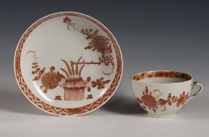  Antique ceramic tableware set consisting of a round plate and a teacup, both featuring an off-white background with intricate rust-colored floral patterns and geometric borders.