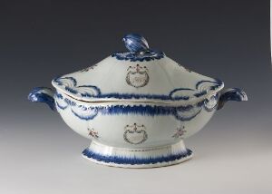  An oval-shaped blue and white ceramic soup tureen with decorative patterns, including floral and heraldic motifs, featuring two handles and a matching lid with a central handle, set against a neutral background. Artist name and title are unknown.