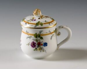  An elegant porcelain sugar bowl with a lid, featuring a white background adorned with colorful floral patterns and gold trim, with a leaf-shaped gold finial on top of the lid.