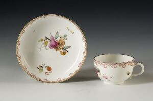  A white porcelain teacup with a handle and a matching saucer, both adorned with hand-painted floral designs in purple, pink, and yellow with green leaves, and edged in gold gilt.