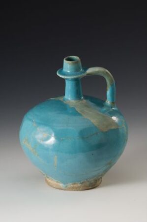  A handcrafted ceramic vessel with a bulbous body and narrow neck in a deep turquoise glaze, featuring a single handle and a contrasting unglazed base.