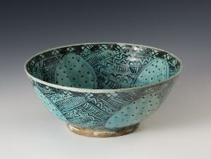  A ceramic bowl with intricate blue patterns on the inside, a lighter blue exterior, and an exposed tan base, set against an off-white background. The bowl is tapered from a wide rim to a smaller base.