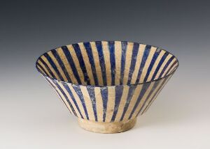  A ceramic bowl with a cream-colored base adorned with vertical cobalt blue stripes, displayed against a soft gray background.