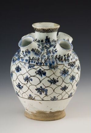  A traditional blue and white ceramic vase with two side spouts and curled handles, featuring intricate blue floral patterns on a white background and an unglazed clay base. No artist or title information provided.