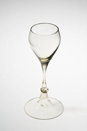  An empty wine glass with a traditional design stands against a white background, displaying clarity and a faint yellowish tinge due to lighting.