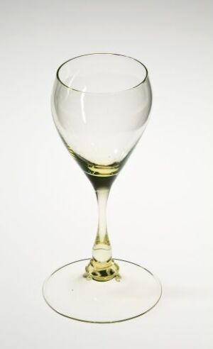  An empty wine glass with a slight green tint on the stem stands against a light grey background, showcasing its clear and simple design with light reflections indicating its glossy texture.