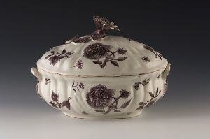  An elegant white ceramic tureen with a scalloped edge and a floral pattern in deep burgundy on a smooth, lustrous surface, featuring a matching lid with a floral finial on top.