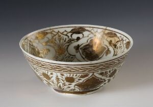  An intricately designed ceramic bowl with floral and abstract patterns in earthy brown, tan, and muted yellow shades on an off-white background, featuring a glossy finish, set against a neutral gray backdrop.