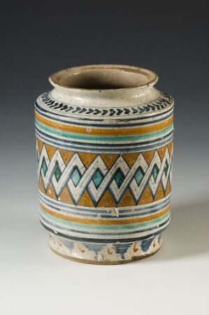  A cylindrical ceramic vessel with a cream base color, decorated with intricate geometric patterns in dark blue and orange, featuring triangles, diamonds, zigzags, and petal-like shapes, all outlined in black.