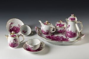  A porcelain tea set with a floral pattern in shades of magenta and purple, accented with gold trim, against a light grey background. The set includes a teapot, sugar bowl, creamer, serving tray, and cups with saucers.