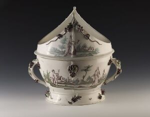  A decorative ceramic tureen with intricate gray monochrome pastoral and floral designs on a creamy white background, featuring two scroll handles and a matching lid with an ornate finial.