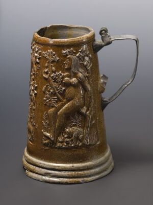  An antique brown stoneware stein titled "Syndefallet" with a pewter handle. The stein features relief art possibly depicting the biblical Fall of Man, with earth-toned hues ranging from golden to dark brown and a reflective salt glaze finish. The artist name is unidentified.