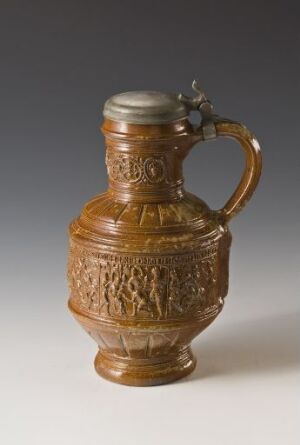  An ornately embossed brown pitcher with a glossy finish, featuring a detailed relief design, a curvy handle, and an hinged lid, set against a neutral gray background.