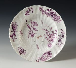  An elegantly decorated ceramic plate with scalloped edges and a floral pattern in shades of purple on a white background.