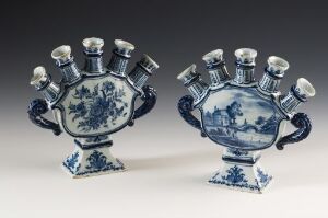  A pair of blue and white ceramic mantel garnitures, possibly Delftware, with ornate landscape scenes and decorative elements, featuring seven candle-holder arms on top and large curving handles on the sides.