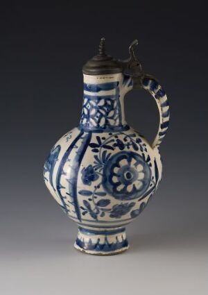  A traditional blue and white ceramic jug with a metallic lid and arching handle, featuring intricate floral and geometric patterns.