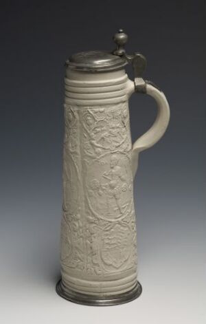  A tall, slender stoneware beer stein with an earthy gray salt-glazed body featuring raised baroque-style relief decoration. The stein has a cast pewter lid and foot, providing a metallic contrast to the textured body. The lid is topped with a small pewter finial, and it has a curved pewter handle for gripping. (Title: David, Artist: Unknown)