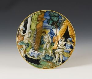  A majolica plate entitled "Venus som bedrar sin ektemann Vulkan med krigsguden Mars," featuring a vibrant, multi-colored mythological scene with classical figures amidst architectural elements and draperies in yellow, green, blue, and white hues.