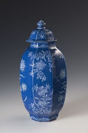  An intricately patterned blue and white porcelain jar with a rounded lid, featuring detailed floral decorations, against a soft gray background.