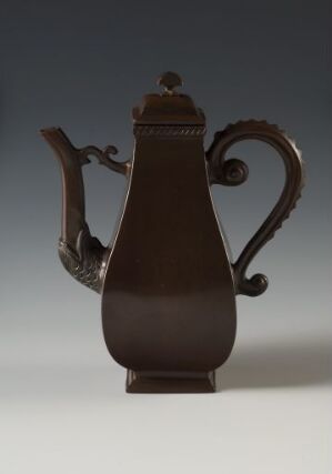  A chocolate brown traditional coffee or tea pot with a matte finish, featuring an elaborate handle and a smooth, dome-shaped lid, set against a subtly graduated gray background.