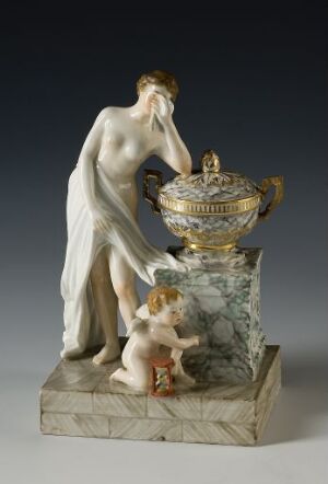  "Sørgegruppe" - A porcelain decorative sculpture with an adult female figure in mourning pose and a cherubic child, beside an ornately patterned urn with gold, blue and floral decoration, all mounted on a rectangular porcelain base.