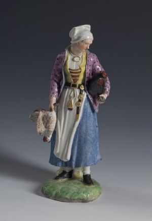  A porcelain figurine titled "Hønsepige," depicting a woman in traditional European peasant attire holding a chicken and a basket, with intricate patterns on her purple jacket, a striped apron over a blue skirt, and a white headscarf, standing on a grass-like base.