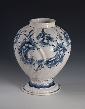  A white-glazed faience vase with hand-painted cobalt blue floral and scroll-like motifs. The vase has a bulbous body with a narrow neck and flared opening, sitting on a small rounded base. Artist unknown.