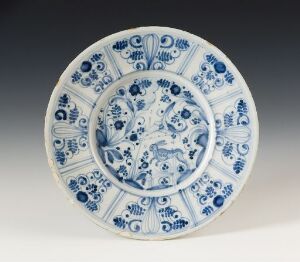  A blue and white porcelain plate with a central circular medallion featuring a deer-like figure surrounded by intricate vegetal patterns, bordered by smaller circular motifs along the sloping edge.