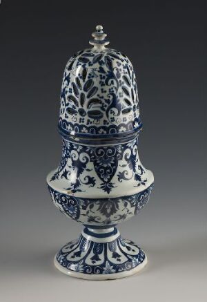  An elegant blue and white porcelain container with a lidded top and a finial, standing on a stemmed foot, displaying intricate floral and scrollwork patterns, displayed against a gray background.